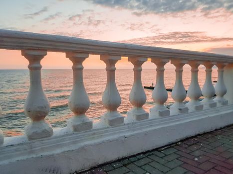 Classic white plaster balustrade on the background of a calm sea at sunset - a delicate pink mood.