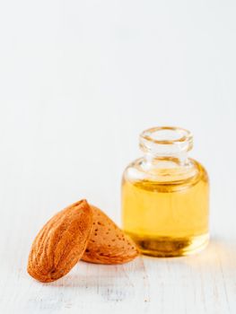 Small glass bottle of almond oil and almonds on white wooden tabletop with copy space. Vertical