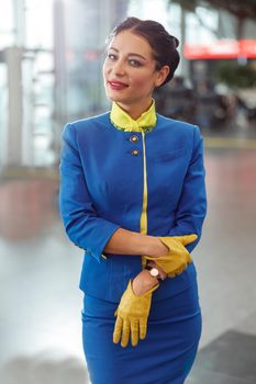 Woman flight attendant wearing blue aviation uniform and gloves while looking at camera and smiling