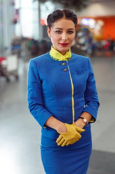 Woman stewardess wearing blue aviation uniform and gloves while looking at camera and smiling
