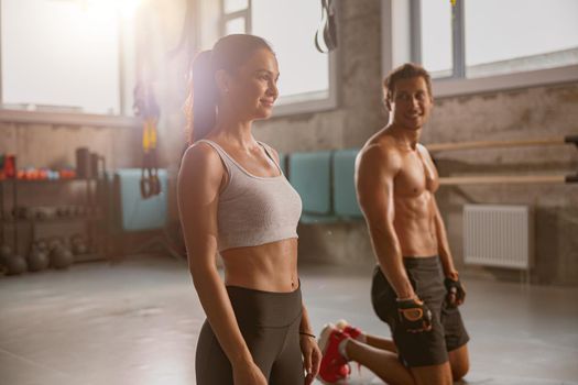 Sporty smiling lady and young man standing on yoga mat in the gym and preparing for workout