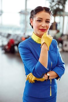 Joyful woman air hostess in aviation uniform looking at camera and smiling while touching her chin