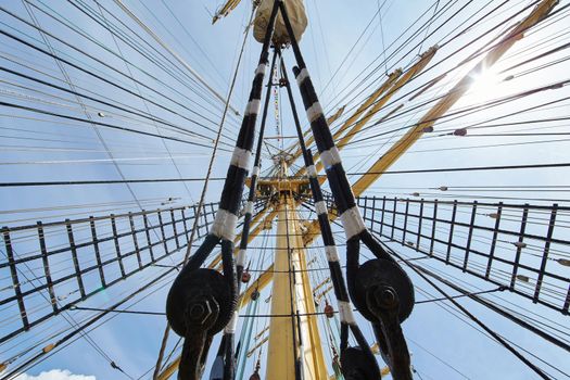 a view from below of the huge mast of an old sailing ship, many ropes hanging down from above, blue sky in the background on a sunny day. High quality photo