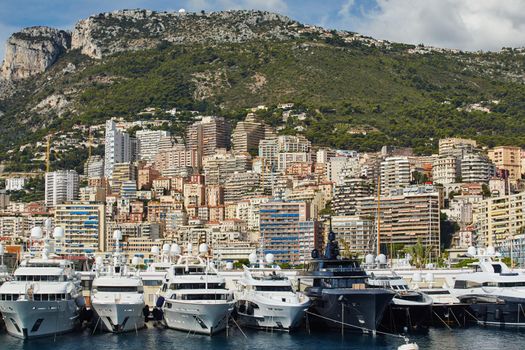 Monaco, Monte-Carlo, a lot of large motor yachts are parked side by side in the port, with huge fenders between them to avoid collision at sunny day, mooring ropes go into the azure water. High quality photo