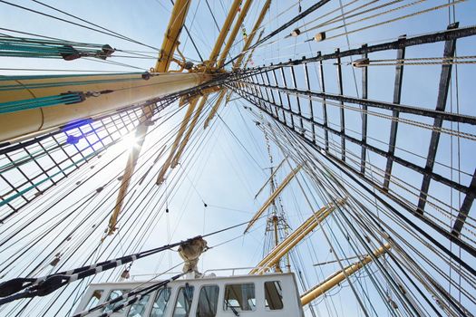 a view from below of the huge mast of an old sailing ship, many ropes hanging down from above, blue sky in the background on a sunny day. High quality photo