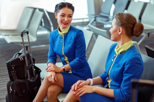 Women stewardesses with travel bags wearing aviation air hostess uniform while waiting for airplane at airport