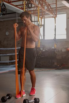 Fully concentrated athletic man performing exercises using resistance band during training in sports club