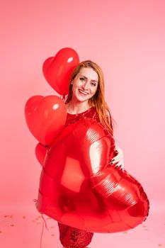 Beautiful redhead girl with red heart baloon posing. Happy Valentine's Day concept. Studio photo of beautiful ginger girl dancing on pink background.