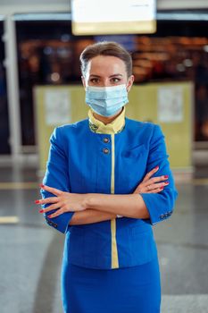 Woman flight attendant wearing protective face mask and aviation air hostess uniform while standing at airport during pandemic