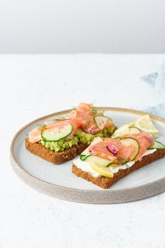 Smorrebrod - traditional Danish sandwiches. Black rye bread with salmon, cream cheese, cucumber, avocado on a wooden background, vertical