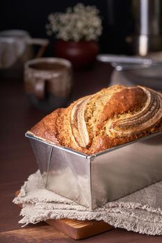 Banana bread in loaf pan. Cake with banana, traditional american cuisine. Whole loaf. Dark background, black table, shadows. Side view, close up.