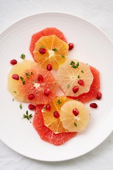 Bright mix of citrus fruits, vertical. Salad of mix sliced round slices of red and white grapefruit sprinkled with pomegranate seeds on white plate.