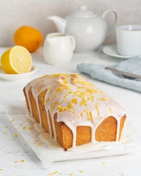 Lemon bread coated with sugar sweet icing and sprinkled with lemon peel. Cake with citrus, poppy, traditional american cuisine. Whole loaf. White background, side view, close up, vertical