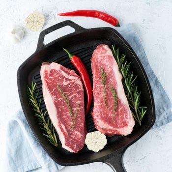 Two fresh raw big whole pieces of meat, beef fillet, marble striploin in cast-iron large pan. Top view, close up. Seasoning steak with salt.