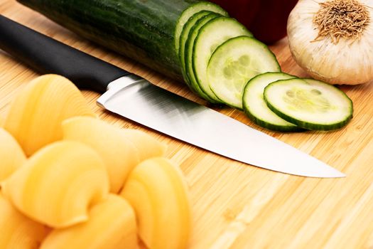 Chopped cucumber on wooden cutting board with knife and assorted fresh vegetables. Diet and vegetarian food preparing, meal cooking concept, healthy lifestyle.