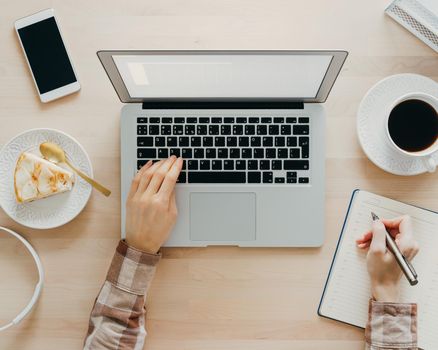 Work from home, online learning. Wooden desk. Top view. Distance education. Woman hands typing on laptop. Freelancer, Digital nomad concept. Dessert with coffee on table