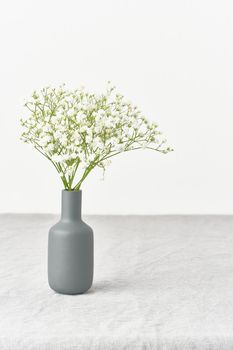 Gypsophila flowers in a vase. Soft light, Scandinavian minimalism, white walls, gray table. Empty space for text. Spring still life, vertical