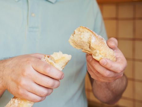Man breaks off hunk of fresh baked homemade crusty bread baguette. Delicious and healthy homemade cakes. Hands close-up. Home atmosphere, cuisine.