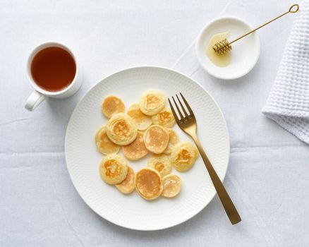 Tiny pancakes, small thin funny crumpet, children's food. Breakfast, white tablecloth, bright morning, top view