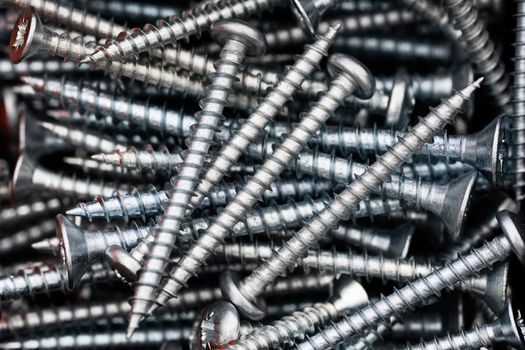 Close up of a pile of multipurpose metal screws. Industrial and construction concept. Metal screw, iron screw, chrome screw.