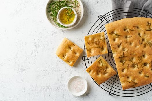 Focaccia, pizza, italian flat bread with rosemary and olive oil on grid on white rustic table, tradition italian cuisine, top view, copy space