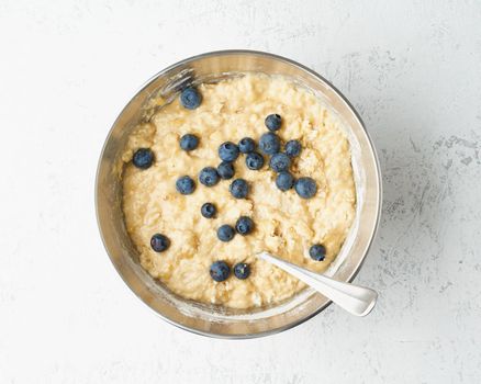 Homemade Banana bread. Dough for cake. Step by step recipe. Step 10. Blueberries and mixed banana with sugar, eggs, yogurt and flour. Top view, white table.