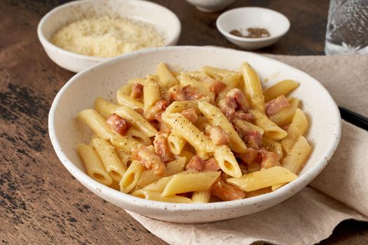 Carbonara pasta. Penne with pancetta, egg, parmesan cheese and cream sauce. Traditional italian cuisine. Side view, close up