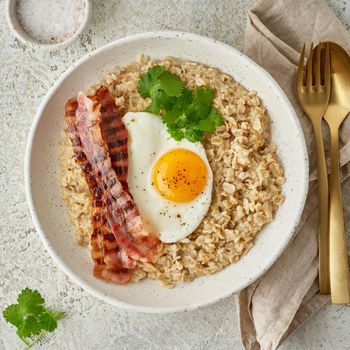 Oatmeal, fried egg, fried bacon. Hearty fat high-calorie breakfast, source of energy. Balance of proteins, fats, carbohydrates. Balanced food. Intuitive conscious food, top view