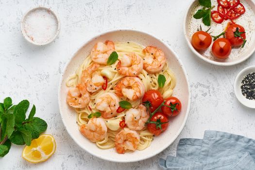 Pasta bavette with fried shrimps, bechamel sauce, mint leaf, garlic, tomatoes, chili on white plate, top view, italian cuisine.