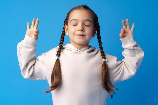 Little girl with braids standing in zen pose against blue backgorund, close up