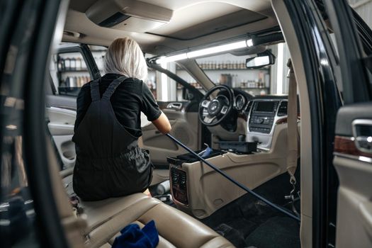 Worker woman vacuum cleaning dust interior inside car in car wash, close up