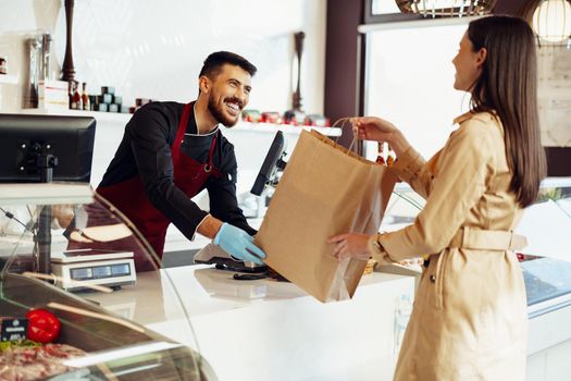 Shop assistant handling shopping bag to female customer in grocery store, close up