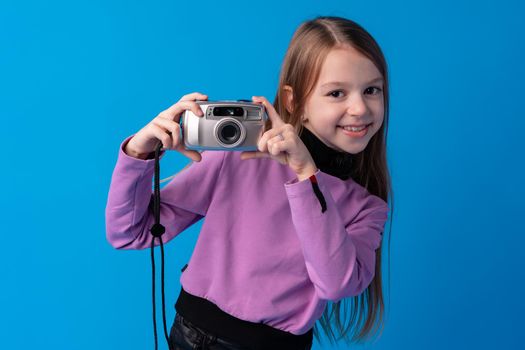 Portrait of a little girl with camera against blue background, close up