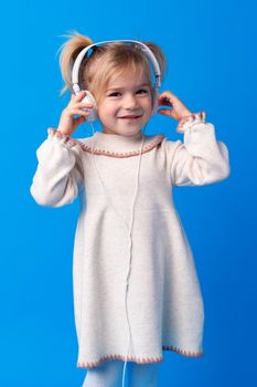 Little girl child wear headphones listen to music over blue background, close up