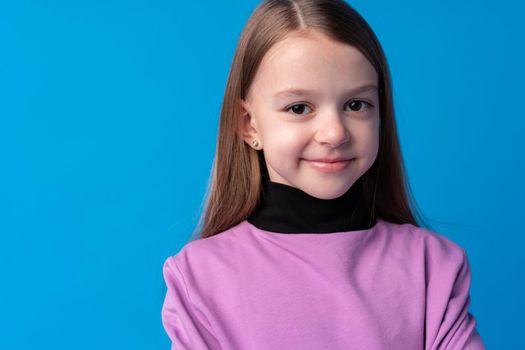 Portrait of a little smiling girl preteen on blue background, close up