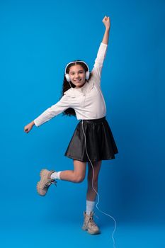 Schoolgirl with headphones listening to music against blue background, portrait