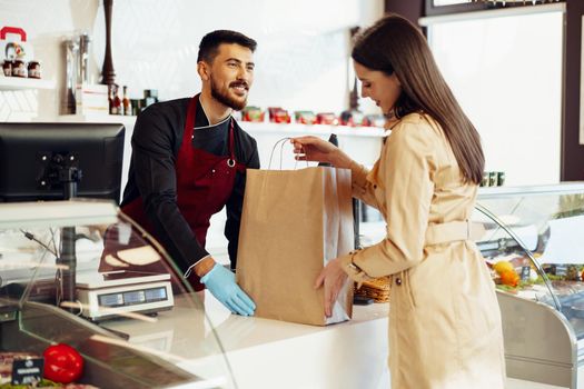 Shop assistant handling shopping bag to female customer in grocery store, close up