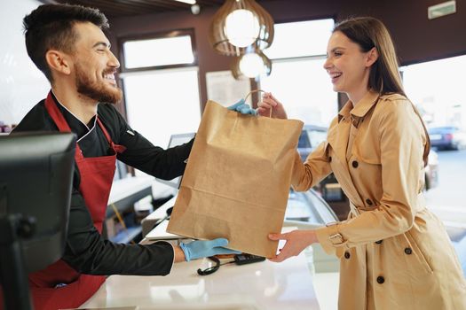 Shop assistant handling shopping bag to female customer in grocery store, close up