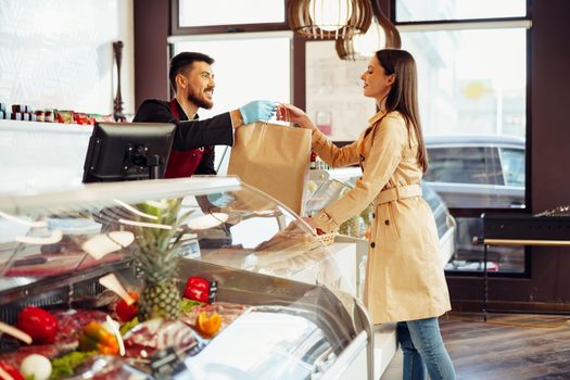 Shop assistant handling shopping bag to female customer in grocery store, close up