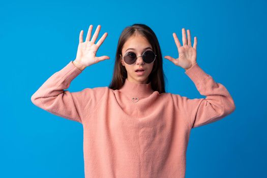 Little fashion girl in sunglasses against blue background, close up