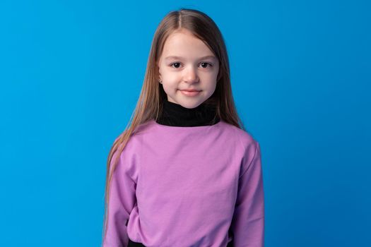 Portrait of a little smiling girl preteen on blue background, close up