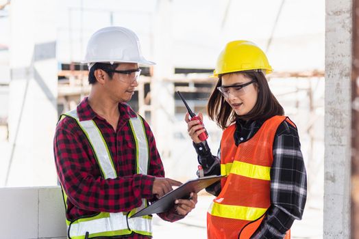 Two Asian engineer foreman architect worker man and woman talking at building construction site, engineering hold radio discussion operate project and control worker employee to building construction