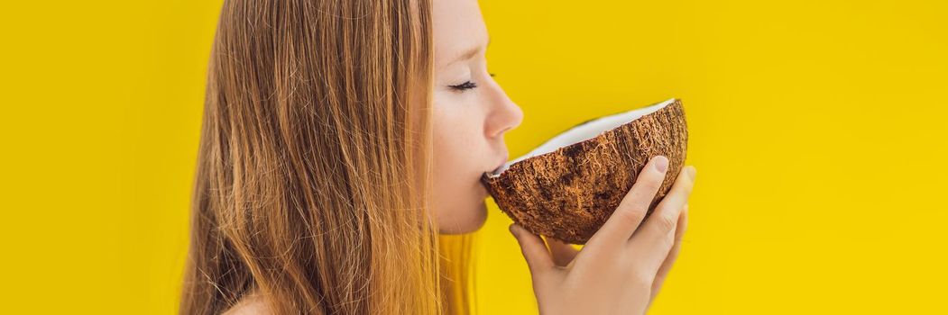 Young woman drinking coconut milk from coconut on a yellow background. BANNER, LONG FORMAT