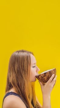 Young woman drinking coconut milk from coconut on a yellow background. VERTICAL FORMAT for Instagram mobile story or stories size. Mobile wallpaper