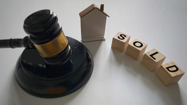 Sold text on wooden blocks with gavel and model house background.