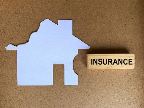 Insurance text on wooden block with burnt model house background.