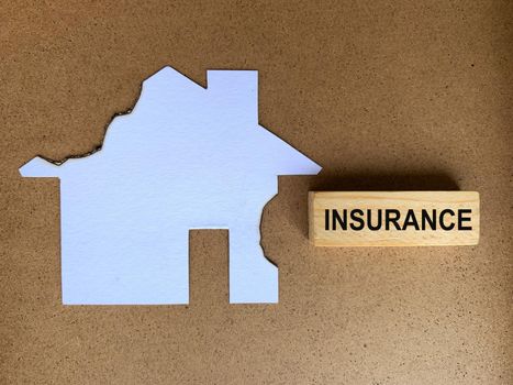 Insurance text on wooden block with burnt model house background.