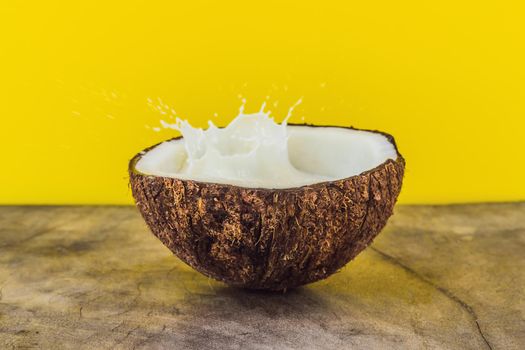 Coconut fruit and milk splash inside it on yellow background.