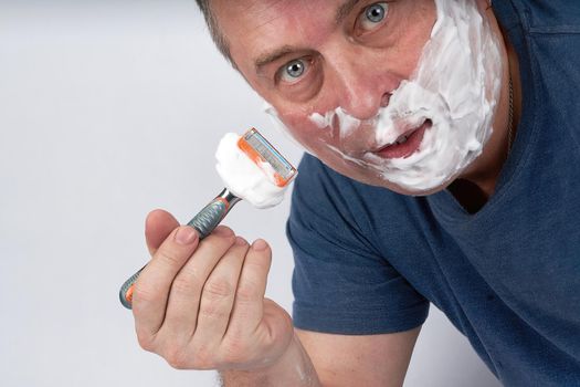 A man's face in shaving foam shaves with a safety razor. Morning or evening exercise, personal hygiene