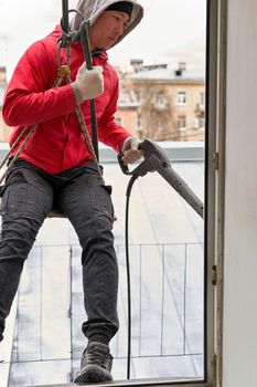 A window washer in climbing gear hangs in the window opening, seen from inside the building